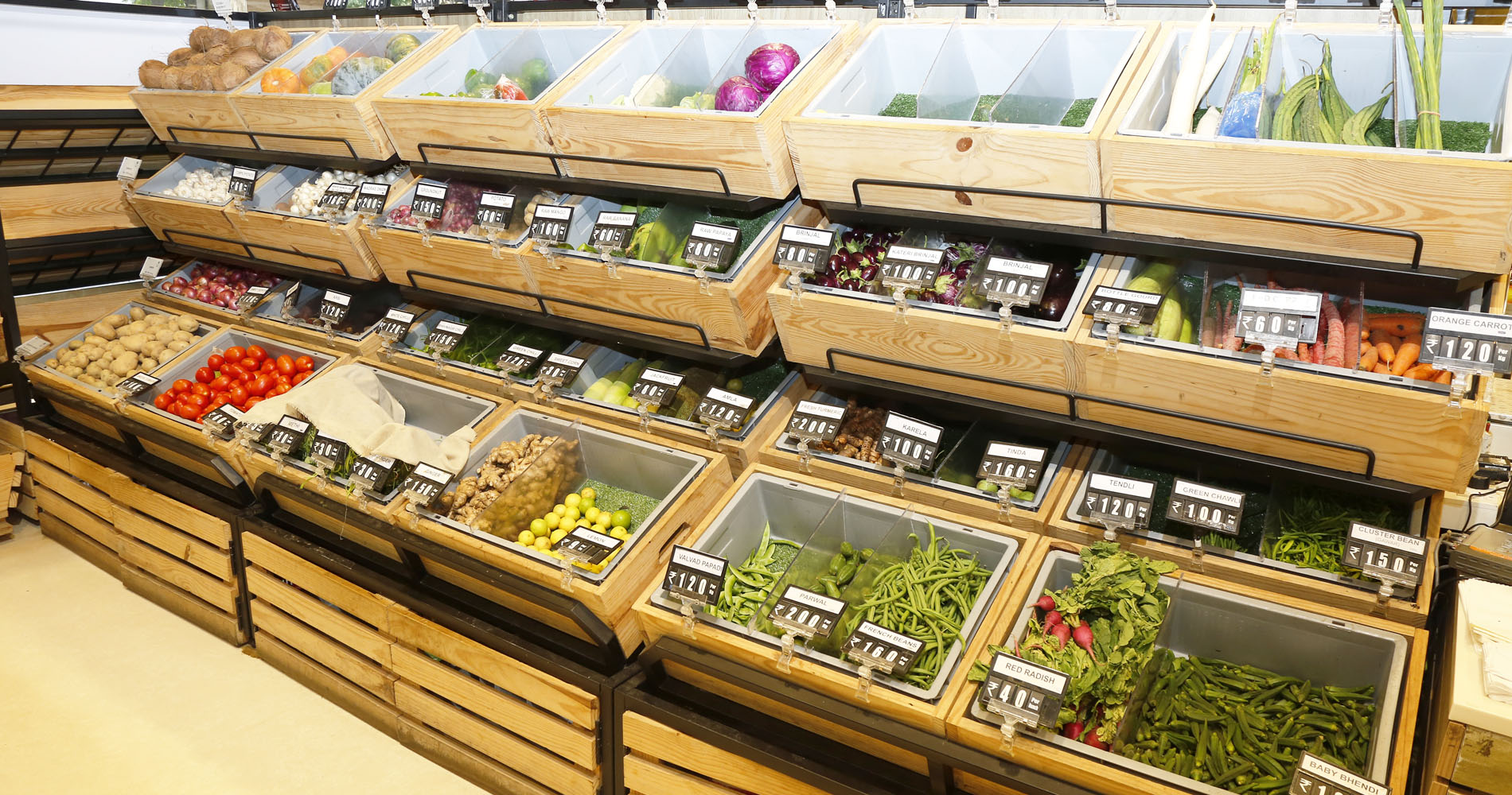 Wooden bulk display bins filled with fresh vegetables in a supermarket produce section.